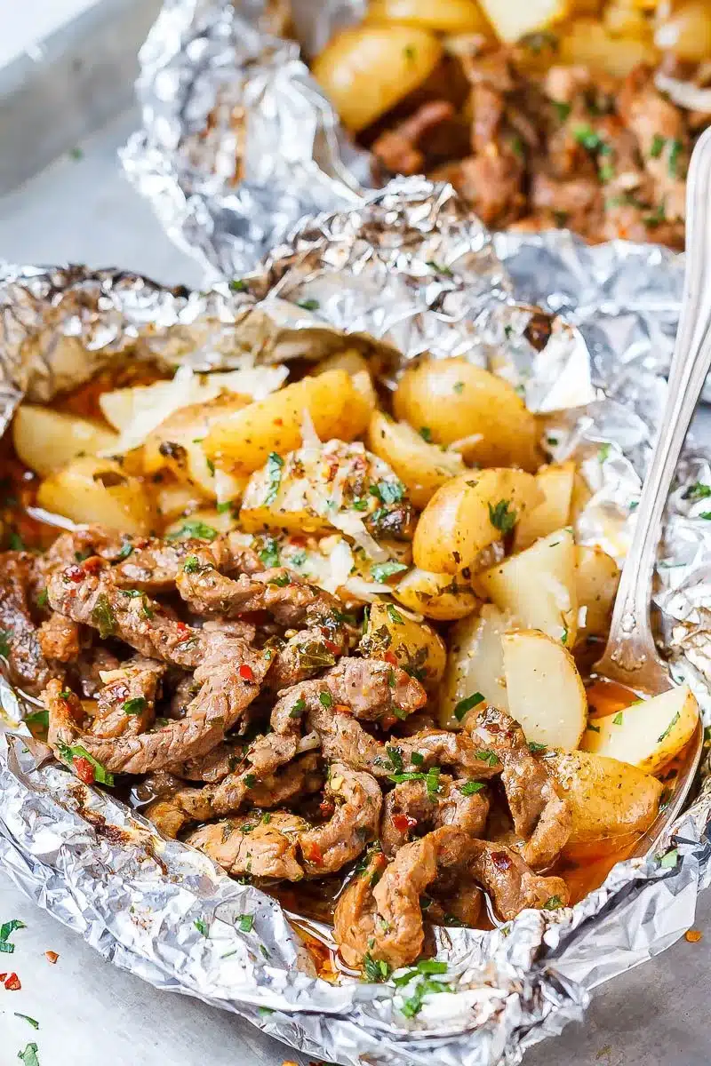 Chunks of steak and small potatoes in a foil packet.