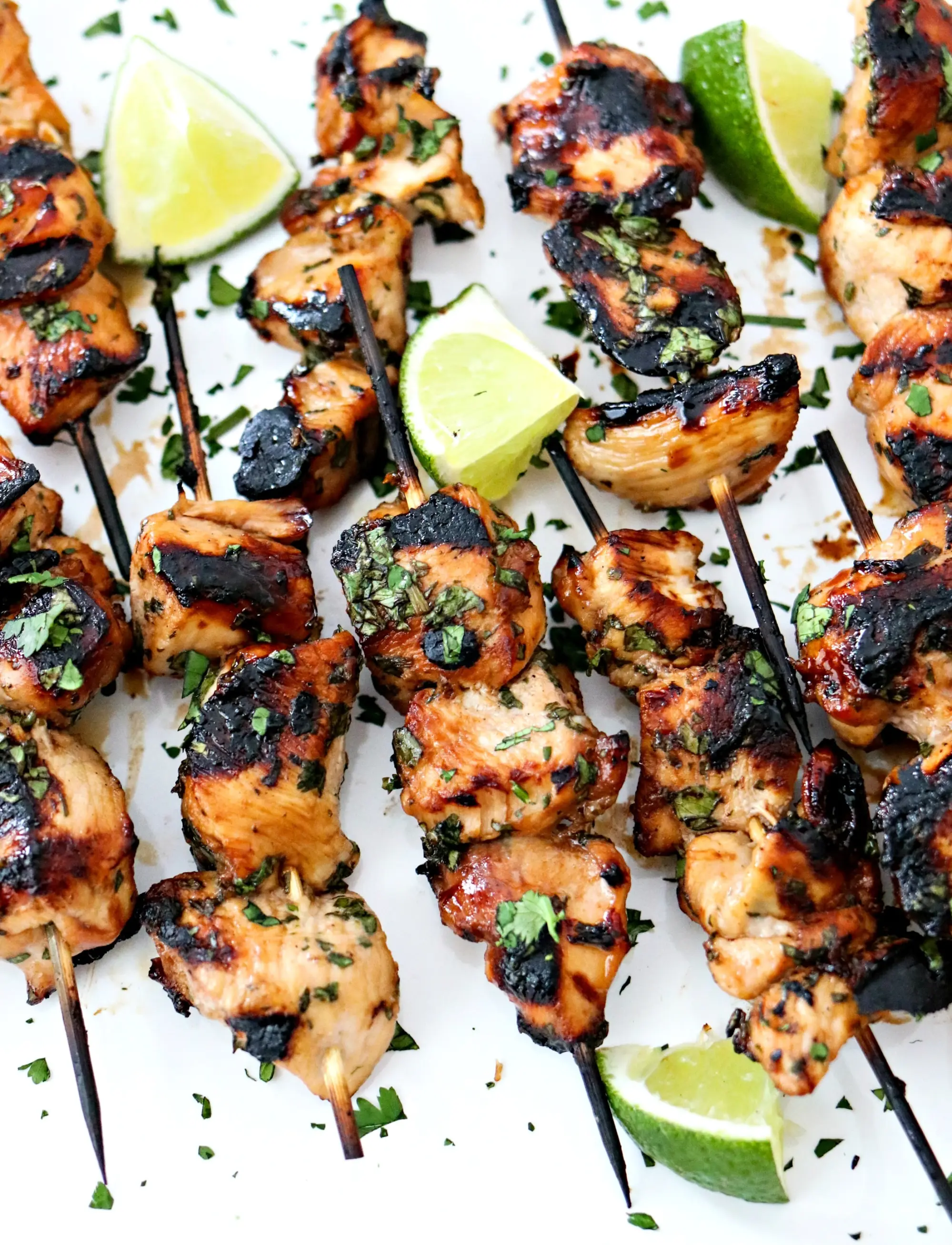 Juicy grilled chicken skewers garnished with fresh herbs and lime wedges on a white plate.