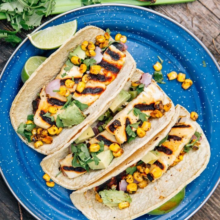 Three tacos filled with grilled halloumi cheese, corn, and avocado on a blue plate