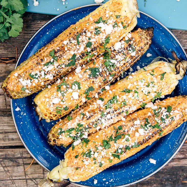 Four ears of corn with crumbled cheese and cilantro on a blue plate