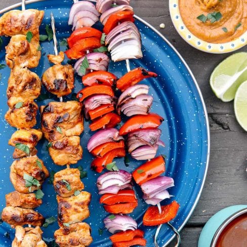 Two grilled chicken skewers next to two grilled pepper and onion skewers on a blue plate.
