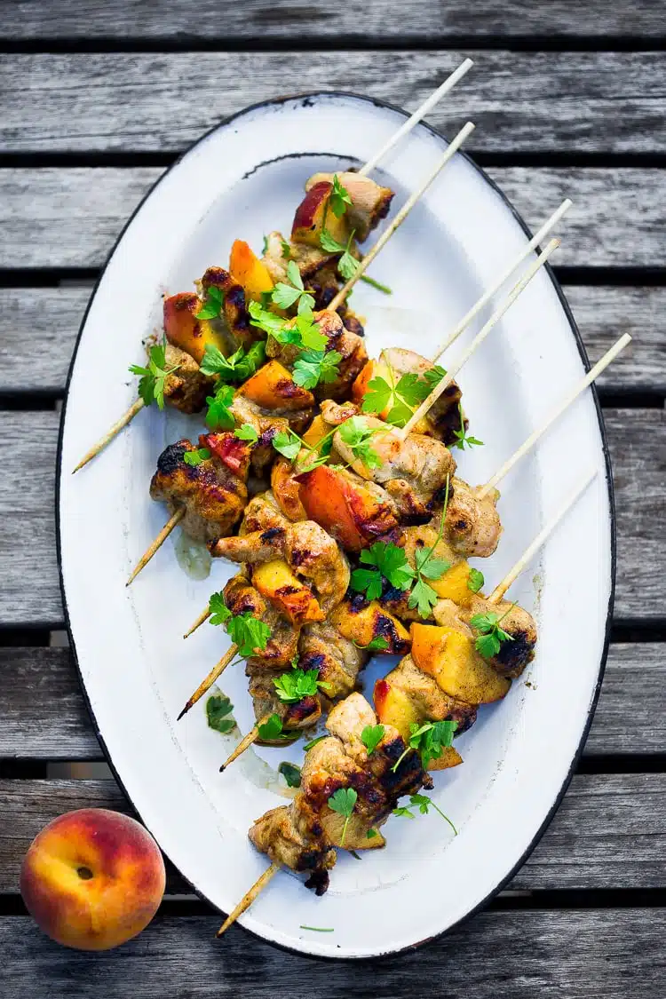 Grilled chicken and peach skewers garnished with fresh cilantro served on an oval white plate, showcasing a delightful blend of savory and sweet flavors.