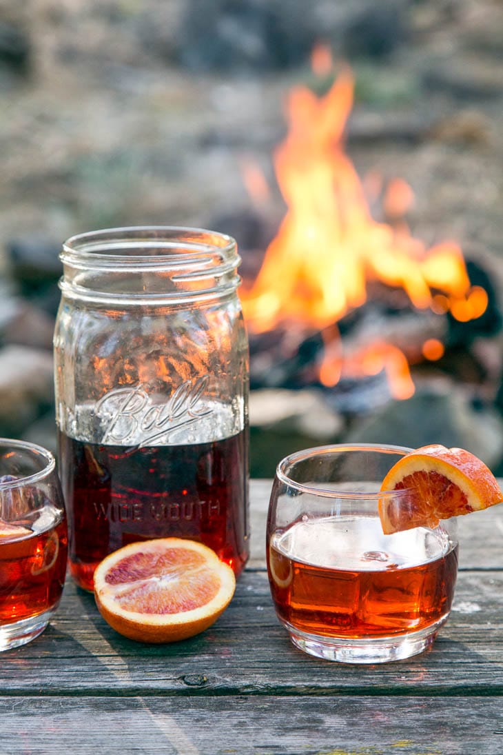 Negroni cocktail in a mason jar on a table in front of a campfire.