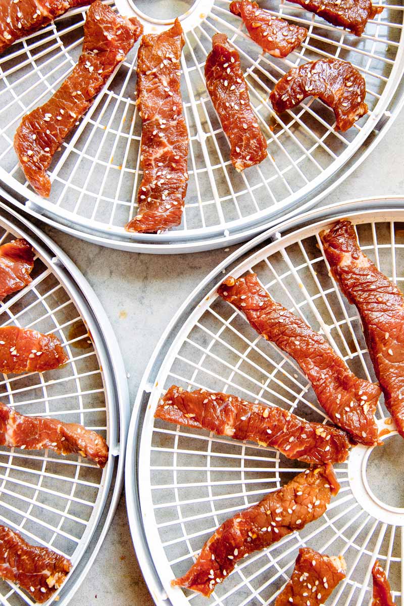 Overhead view of strips of marinated beef on round dehydrator trays.