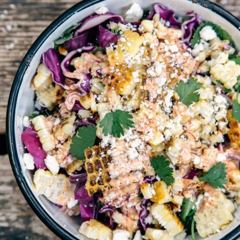 A bowl of grilled corn kernels, crumpled cheese, cilantro, and shredded red cabbage.