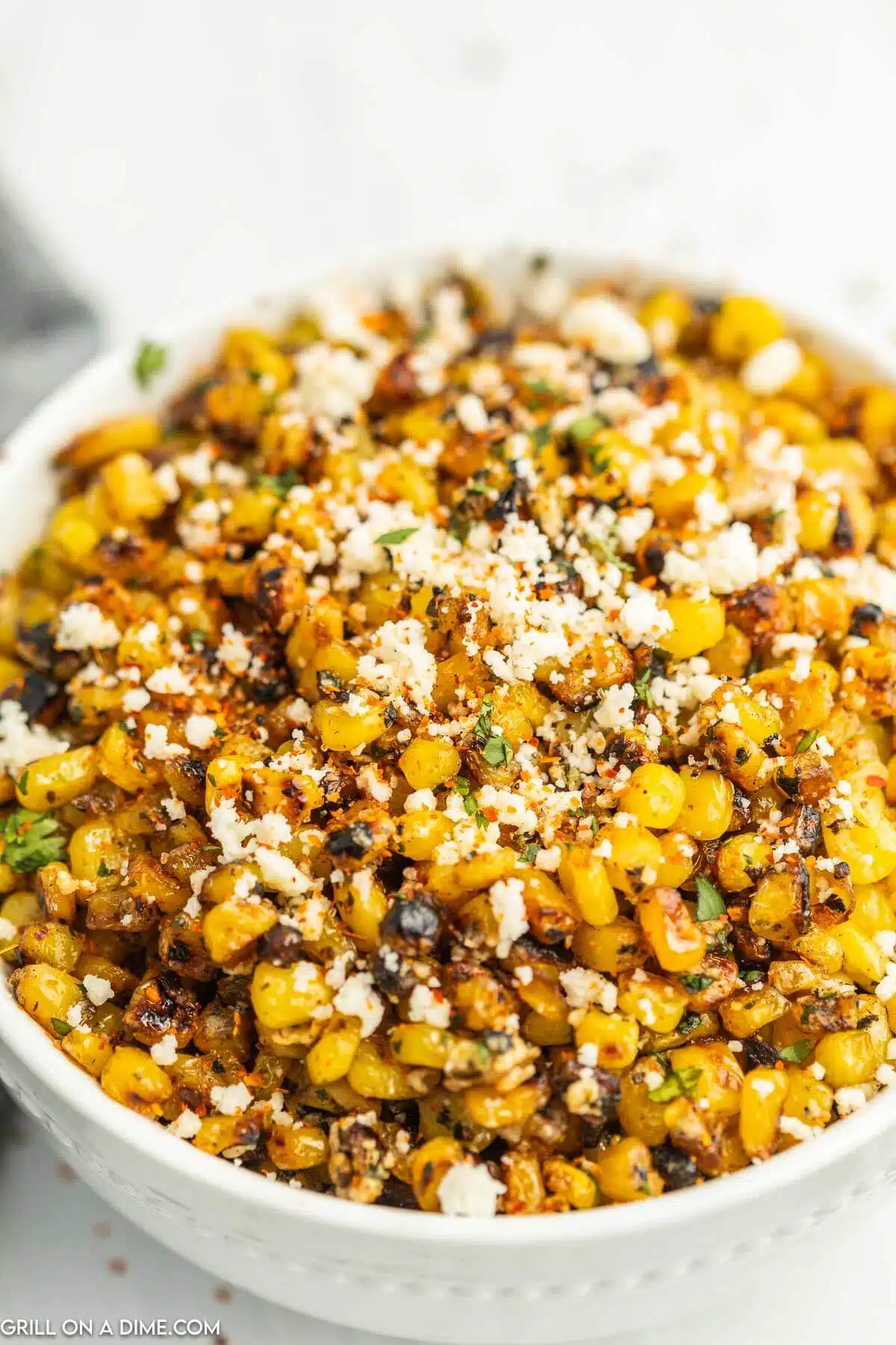 Corn topped with crumbled cheese and spices in a bowl.