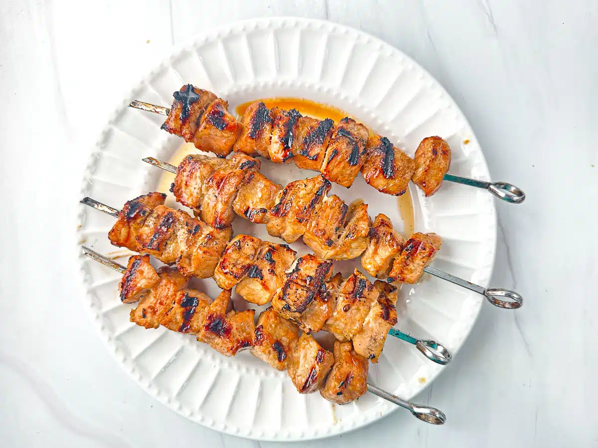 Grilled skewered chicken with appetizing char marks served on a white plate.