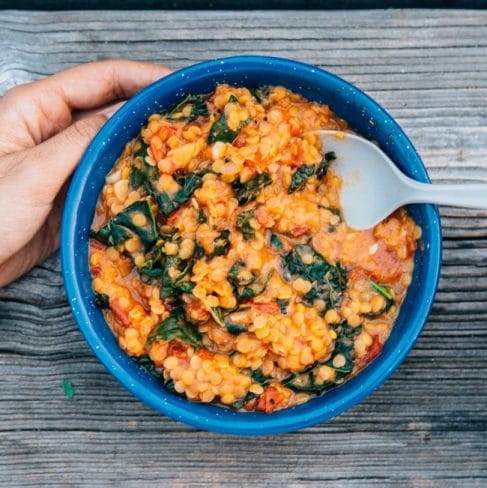Lentil stew and kale in a blue bowl with hands in frame