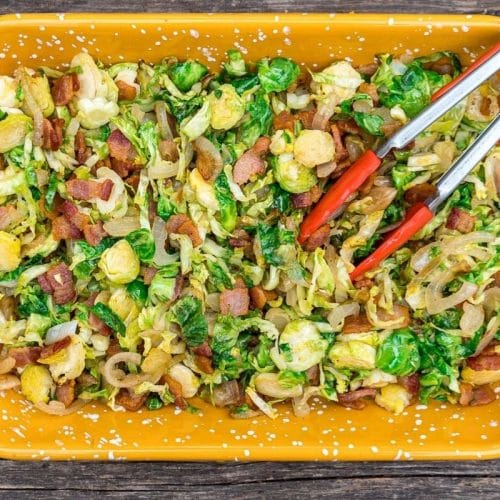 Shredded brussels sprouts in a yellow dish with red tongs
