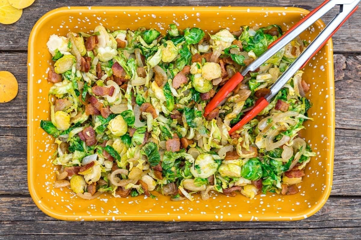 Shredded brussels sprouts in a yellow dish with red tongs