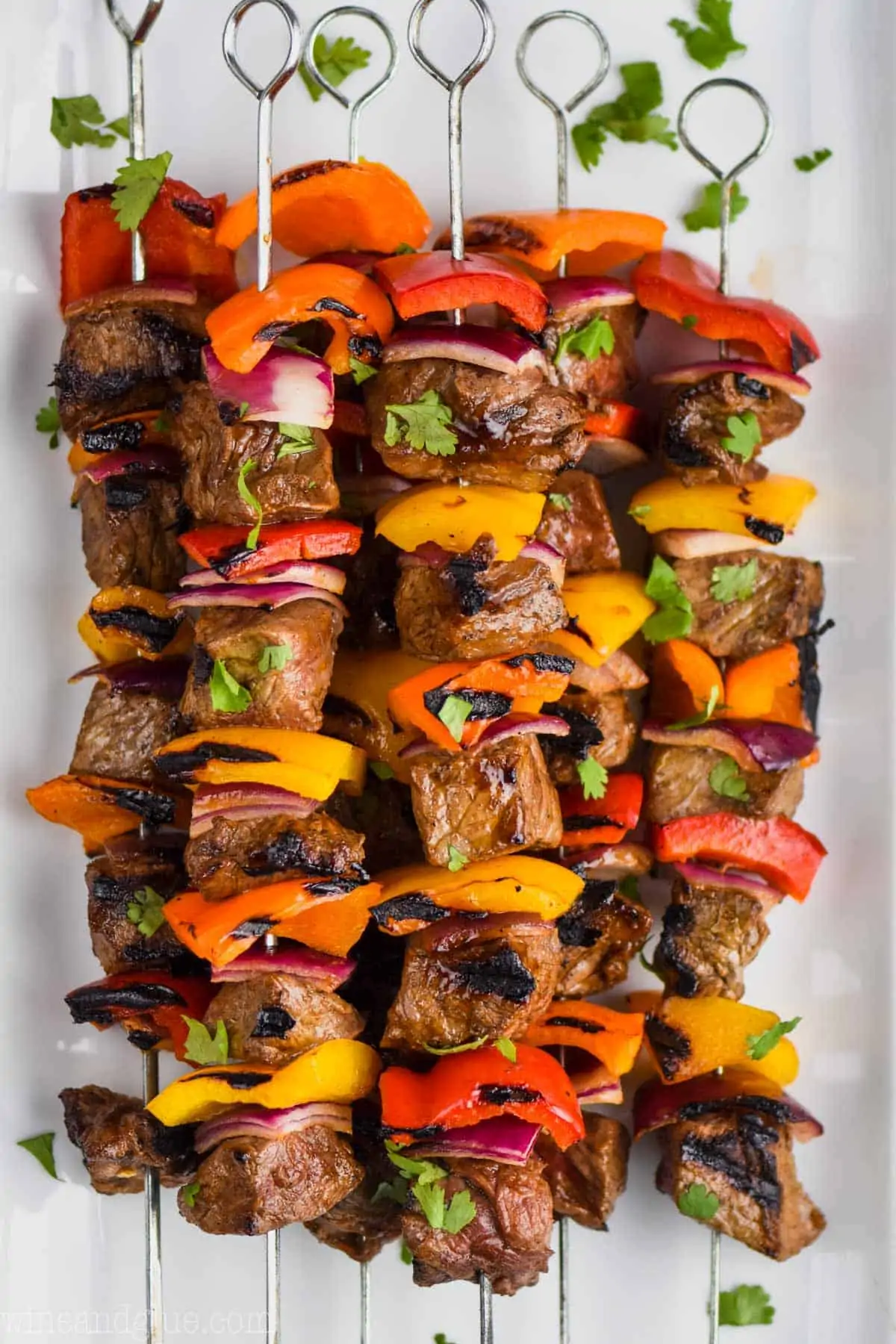 Grilled beef and vegetable skewers garnished with fresh herbs on a white platter.