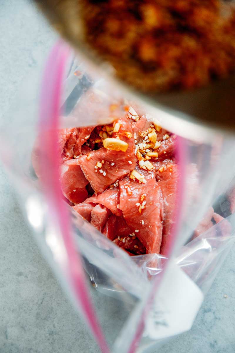 Overhead view of jerky marinade being poured into a bag with sliced beef.