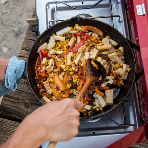 Stirring a medley of colorful vegetables and tofu in a skillet over a camp stove, capturing the essence of delicious outdoor cooking.