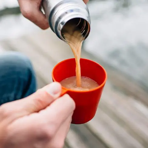 Pouring a tea latte from a thermos into a small red cup