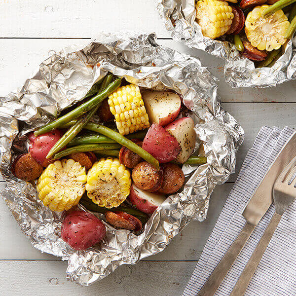 Chunks of potatoes, corn, sausage, and green beans in foil packs.
