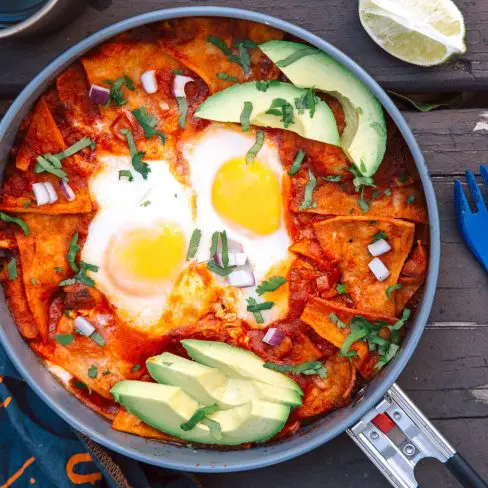 A skillet with chilaquiles, two eggs, and sliced avocado