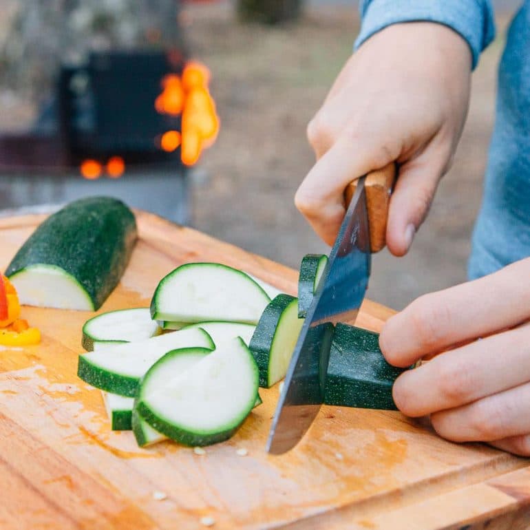 Megan slicing a zucchini with a campfire in the background