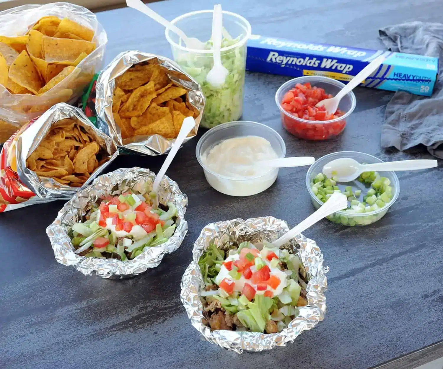 Foil packets with taco ingredients on a wood table.