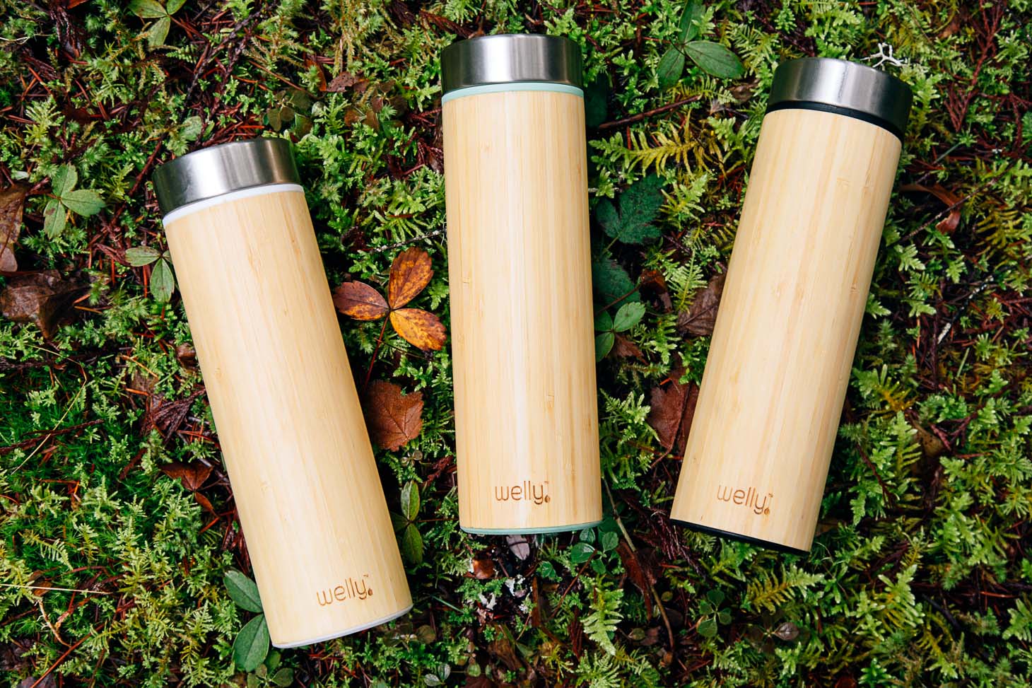 Three bamboo water bottles on a mossy surface.